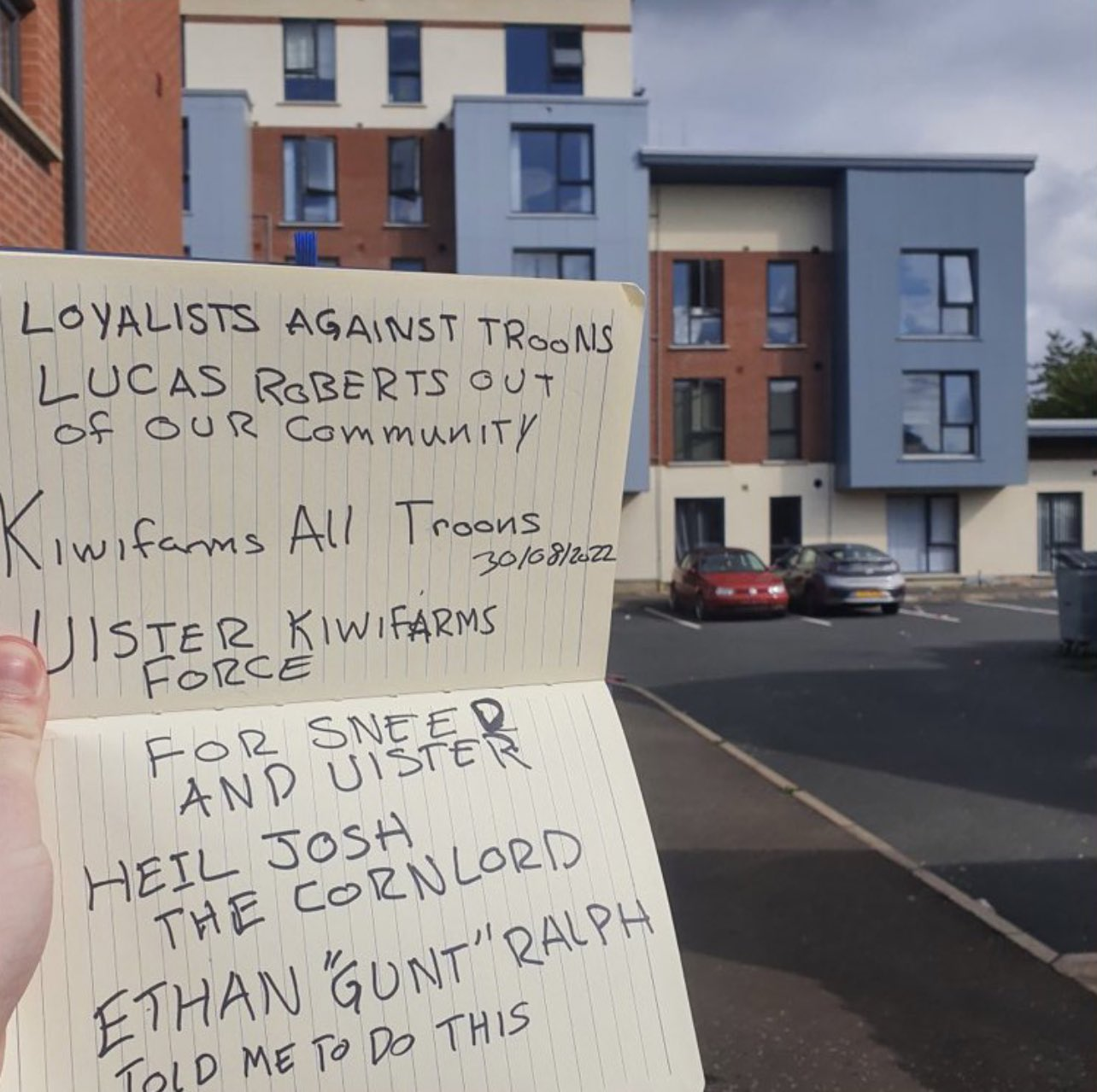 A hand holding a letter outside a block of flats. Letter reads "Loyalists against troons // Lucas Roberts out of our community // Kiwifarms all troons 30/08/2022 // Ulster Kiwifarms Force // For sneed and Ulster // Heil Josh the cornlord // Ethan "Gunt" Ralph told me to do this"