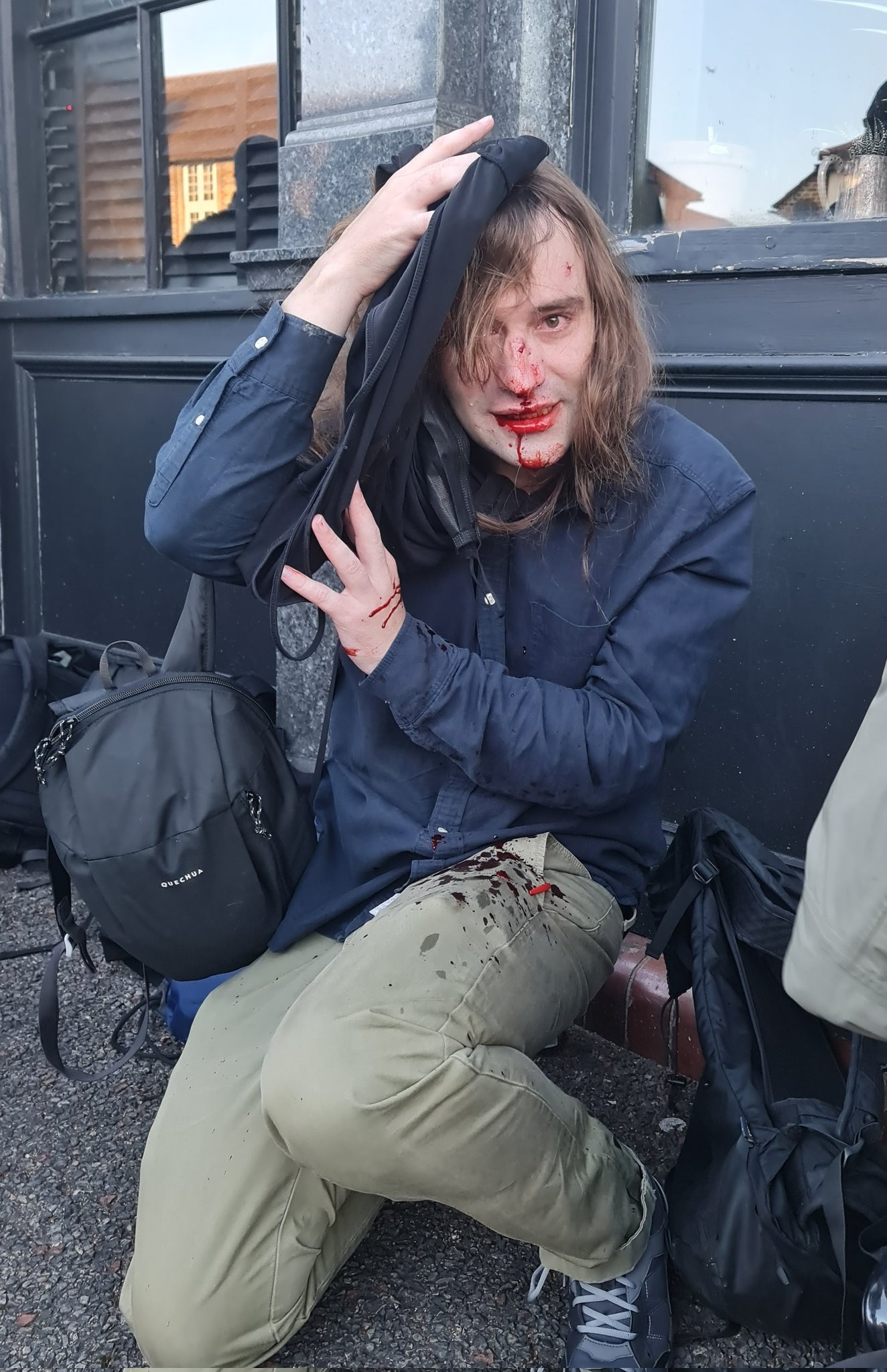 South London activist Ada Cable crouched down, holding a piece of clothing on her head. Blood is streaming down her nose and from her mouth onto her trousers.