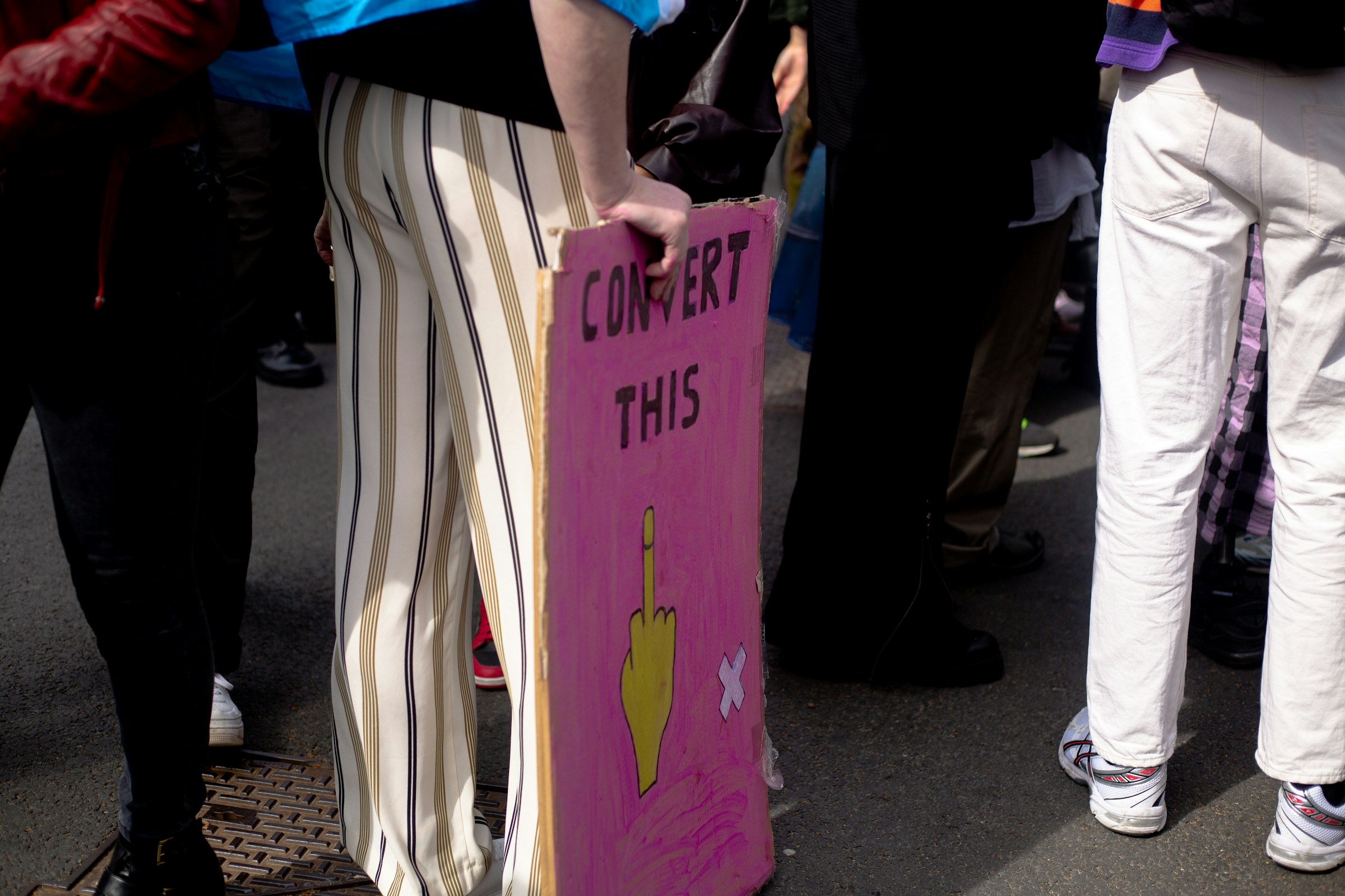 A group of people stood around a pink sign reading “Convert this” with an image of a raised middle finger