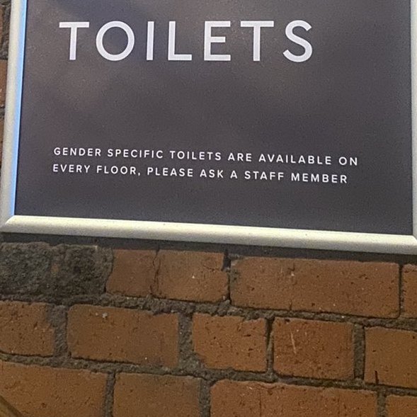 A zoomed in view of a sign directing customers towards toilets. The text reads: 'Gender specific toilets are available on every floor, please ask a staff member'